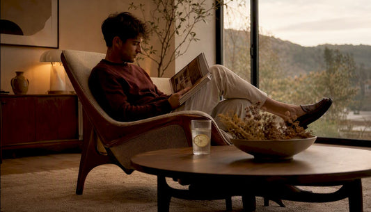 Ein junger Mann sitzt entspannt auf einem stilvollen Mid-Century-Sofa in seinem Wohnzimmer.